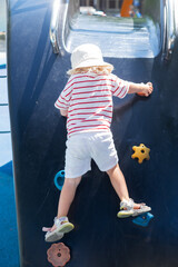 Toddler girl climbing up a slide on a playground