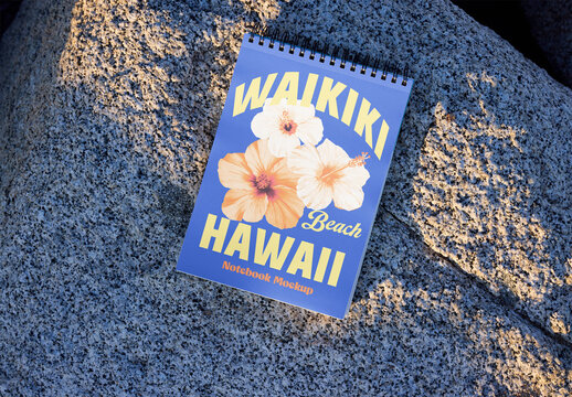 blank ruled spiral notebook mockup rests on a textured rock surface under soft natural light.