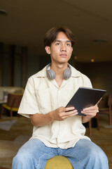 Non binary Asian student man sitting in modern coffee shop using digital tablet computer