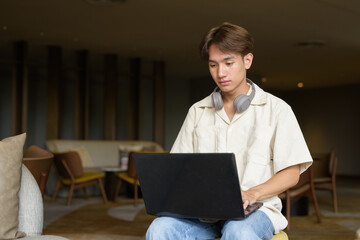 Non binary Asian student man sitting in modern coffee shop using laptop computer