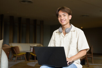 Non binary Asian student man sitting in modern coffee shop using laptop computer