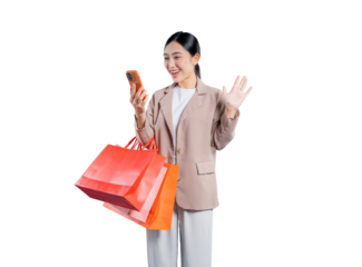 A cheerful young Asian woman holds shopping bags while happily waving at her smartphone, engaged in a friendly video call or live stream, standing against a  png background.
