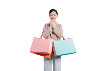 A grateful young Asian woman, holding shopping bags, closes her eyes with a serene smile and clasped hands, feeling thankful and blessed for her purchases, against a png background.
