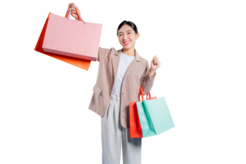 A cheerful and confident young Asian woman smiles while holding up her shopping bags and making a small celebratory fist gesture, expressing her happiness with her purchases.

