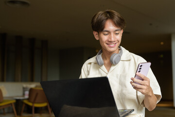 Non binary Asian student man sitting in modern coffee shop using laptop computer