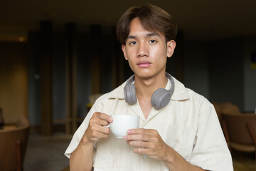 Non binary Asian student man sitting in modern cafe drinking coffee
