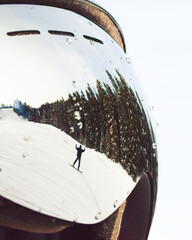 Snowboarder carving snowy slope reflected in ski goggles with water drops, pine forest under clear...
