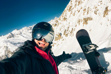 Happy excited snowboarder taking a selfie after reaching top before freeriding in caucasus...