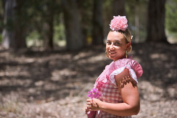 Portrait of young woman, beautiful, blonde, with typical Andalusian flamenco costume to go on pilgrimage with a small shawl and pink flower, with a violet flower in her hands.