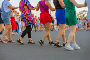 Diverse group of people dancing in colorful summer outfits outdoor , stepping in sync holding arms. Concept of dancing, joy, dancing, street event