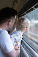 father, traveling with his little toddler by train, looking at the window. 