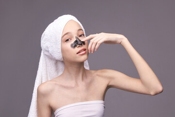 Young caucasian female applying charcoal face mask with towel on head for skincare routine.