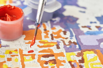 Close up of paintbrush and paint by numbers canvas with vibrant colors.