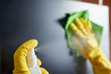 Close up of gloved hands cleaning screen with spray bottle and cloth for a streak free surface.
