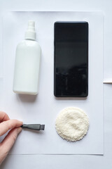 Smartphone cleaning accessories: spray bottle, brush, cloth, and smartphone on white surface.