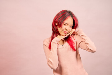 Young woman with red hair making a funny face and winking on pink background