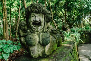 Obraz premium Stone sculpture of a laughing woman with monkeys clinging to her, found in the Sacred Monkey Forest Sanctuary, Ubud, Bali, Indonesia. Tourist attraction.