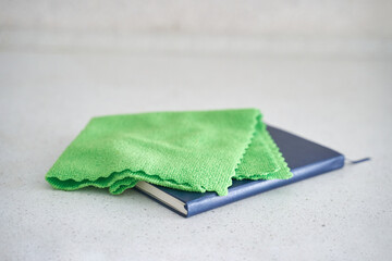 Green cleaning cloth on closed blue notebook on white surface.