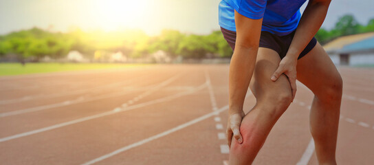 Athlete holding painful red sore calf on running track showing muscle cramp or leg injury during sports training exercise outdoors