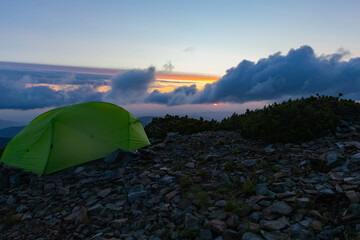 A light green tent on a rocks on top of a mountain against the backdrop of dawn, 