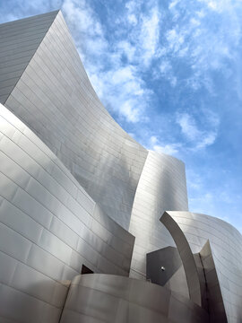 Los Angeles, California, USA - April 18, 2024: Curved stainless steel facade of Walt Disney Concert Hall against blue sky with clouds