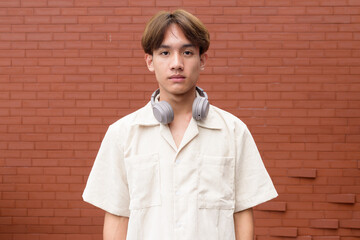 Non binary cute Asian young gay man against brick wall