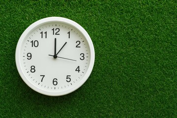 Detailed view of a white decorative clock indicating 10:45 on a textured green surface with empty space