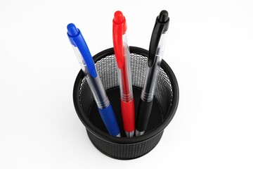 A set of three vibrant gel pens in a pen holder, viewed from above on a white backdrop