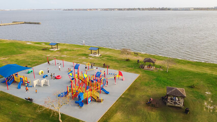 Fototapeta premium Parents and kids enjoy playing at colorful lakefront playground, T-shaped fishing pier stretches into Clear Lake, Seabrook. Scene reflects dynamic lakefront recreation, family-friendly park, Texas