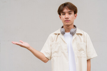 Non binary cute Asian young gay man showing and pointing to copy space