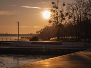A peaceful sunset over the harbor in Senftenberg, Germany. The golden light reflects on the calm...
