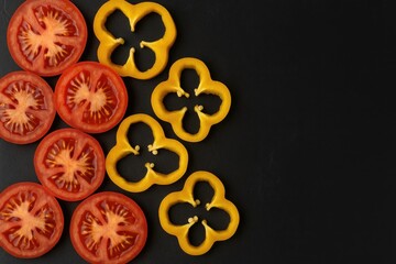 Fototapeta premium Fresh sliced tomatoes and yellow bell peppers on a dark surface with space for writing