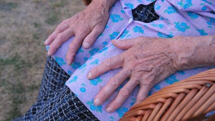 Senior woman’s wrinkled hands resting on lap in outdoor chair 