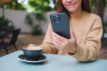 Closeup image of a woman holding and using mobile phone while drinking coffee in the outdoors cafe