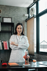 Female doctor in a modern office, wearing a white coat, with anatomical models on the desk.