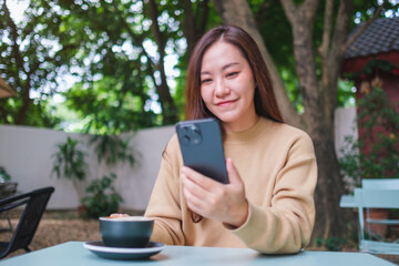 Portrait image of a woman holding and using mobile phone while drinking coffee in the outdoors cafe