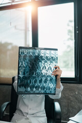 A healthcare worker in a white coat holds an X-ray film in a sunlit office, highlighting medical...
