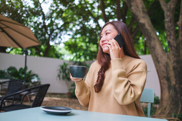 Portrait image of a young woman talking on mobile phone while drinking coffee in the outdoors cafe
