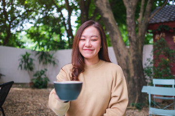 Portrait image of a woman holding and serving a cup of coffee in the outdoors cafe