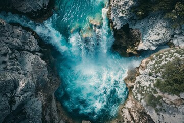 Aerial view of a stunning turquoise waterfall plunging into a narrow gorge, creating whitewater rapids amidst rugged rocks
