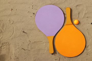 Beach tennis rackets and ball on sand. Active lifestyle, games and sports. Beach tennis set. Bright wooden rackets for outdoor games. Summer outdoor games. Summer sports and games concept. Close-up