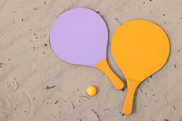 Beach tennis rackets and ball on sand. Active lifestyle, games and sports. Beach tennis set. Bright wooden rackets for outdoor games. Summer outdoor games. Summer sports and games concept. Close-up