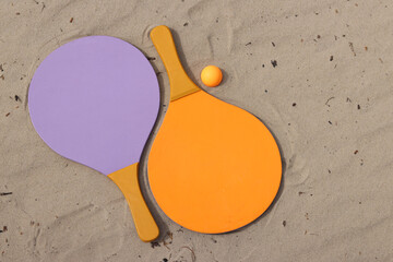 Beach tennis rackets and ball on sand. Active lifestyle, games and sports. Beach tennis set. Bright wooden rackets for outdoor games. Summer outdoor games. Summer sports and games concept. Close-up