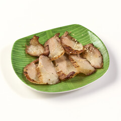 Grilled pork neck slices served on green banana leaf patterned plate, showcasing golden brown texture and garnished with garlic for flavorful and appetizing presentation