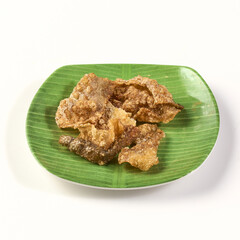 Crispy fried fish skin served on green plate resembling banana leaf, showcasing crunchy texture and golden brown color, perfect as savory snack or appetizer