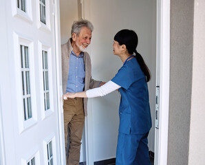 Fototapeta premium Doctor or nurse caregiver woman with senior man at home or nursing home, a caregiver standing on the front door arriving and being welcomed by a senior man