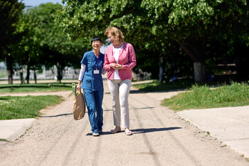 Nurse caregiver with senior woman walking outdoors and helping with shopping bag with groceries
