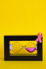 Creative visual of horizontal hourglass filled with pink sand and a pink ribbon attached to the...