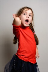 Young girl in red shirt listening intently, mouth open in surprise or excitement. Studio portrait.