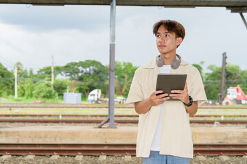 Young non binary tourist traveler in train station using tablet computer